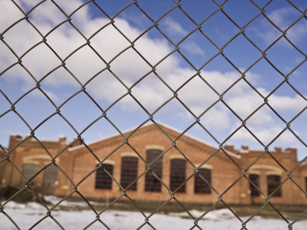 A picture of a chain link fence with a building in the back round looking through the fence
