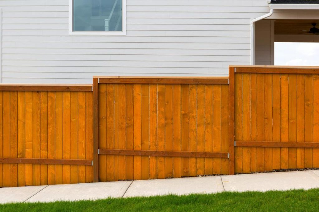 A picture of a fence going up hill next to a house and sidewalk