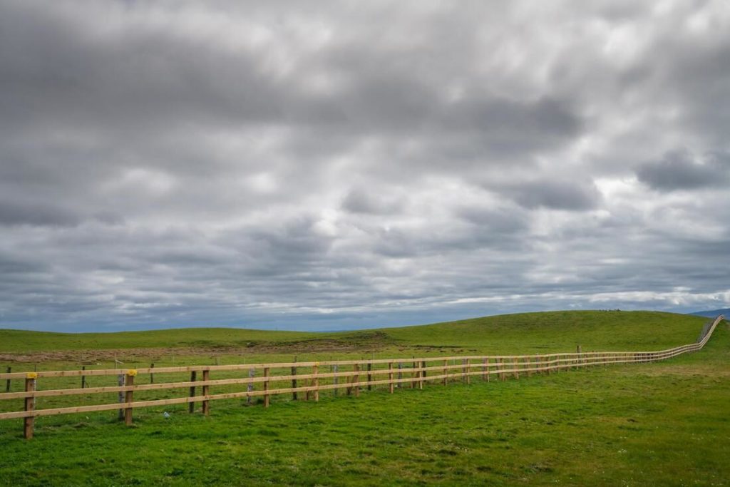 A picture of a split rail fence with a cloudy sky and green grass